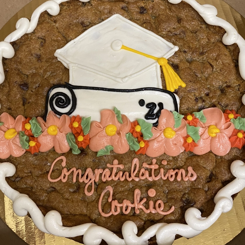 A large cookie from our local bakery decorated with a white graduation cap, pink and orange flowers, and the words "Congratulations Cookie" written in pink frosting.