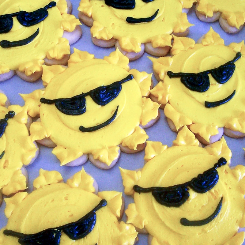 A local bakery crafted a delightful group of cookies decorated as yellow suns wearing black sunglasses with smiling faces.