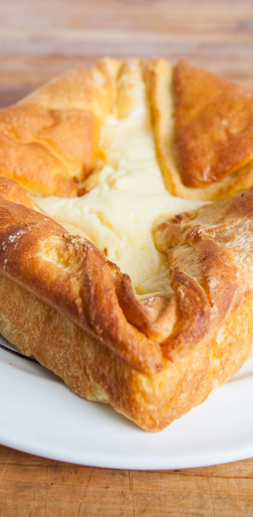 A close-up shot of a baked puff pastry filled with creamy cheese, served on a white plate.
