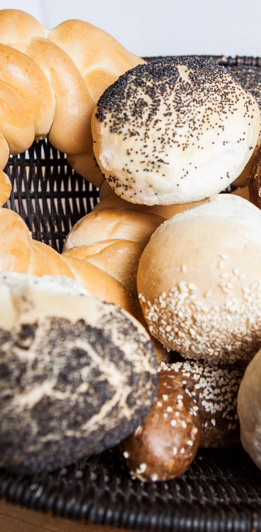 A basket containing a variety of bread rolls, including sesame seed, poppy seed, and plain.