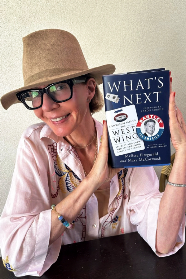 Allison Janney from The West Wing, holding the book "What's Next: A Backstage Pass to The West Wing, Its Cast and Crew, and Its Enduring Legacy of Service."